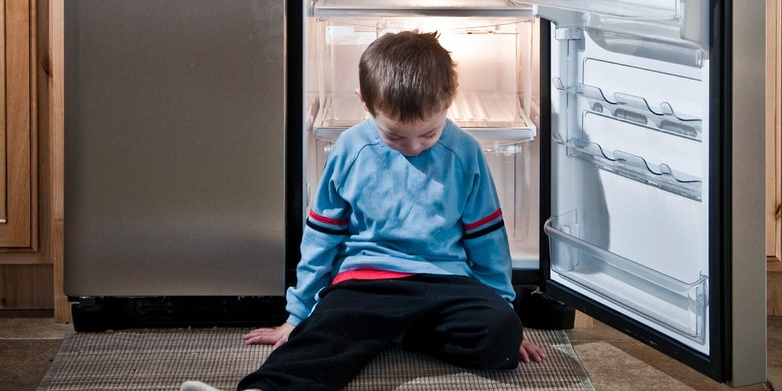 Child sitting in front of an empty fridge