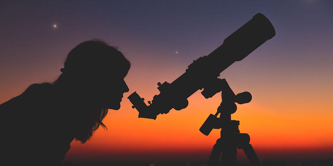 Woman looking down telescope under a night sky