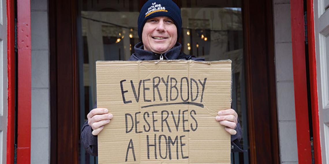 Steve Logan in his 14 Hours Homeless beany holding a sign that says ‘Everybody Deserves a Home