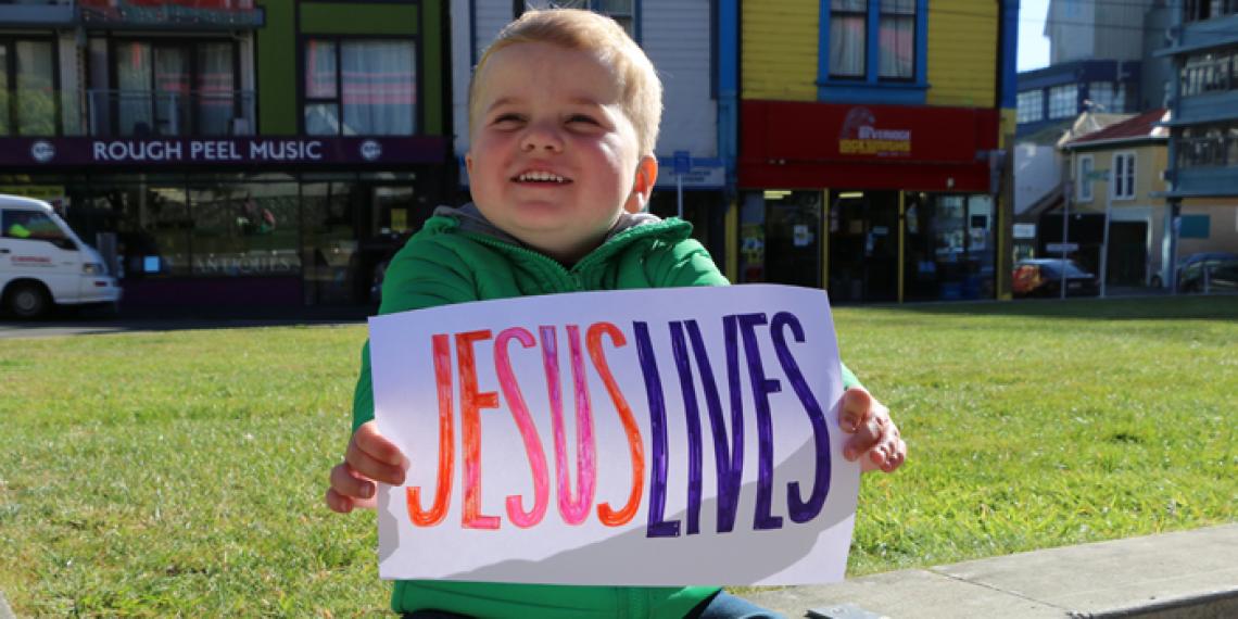 Cute little boy holds a sign saying 'Jesus Lives'